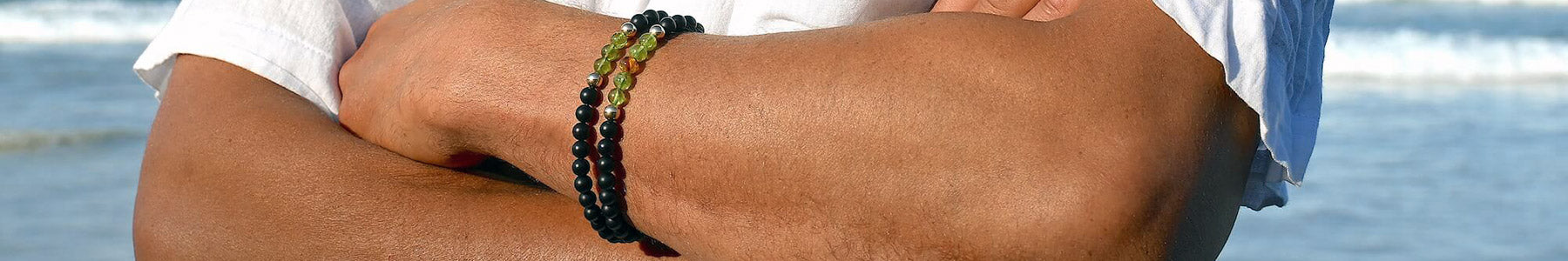 Hero image showing two layered crystal bracelets for men on the wrist with a beach background. Mana for Men Empowerment Jewellery collection.