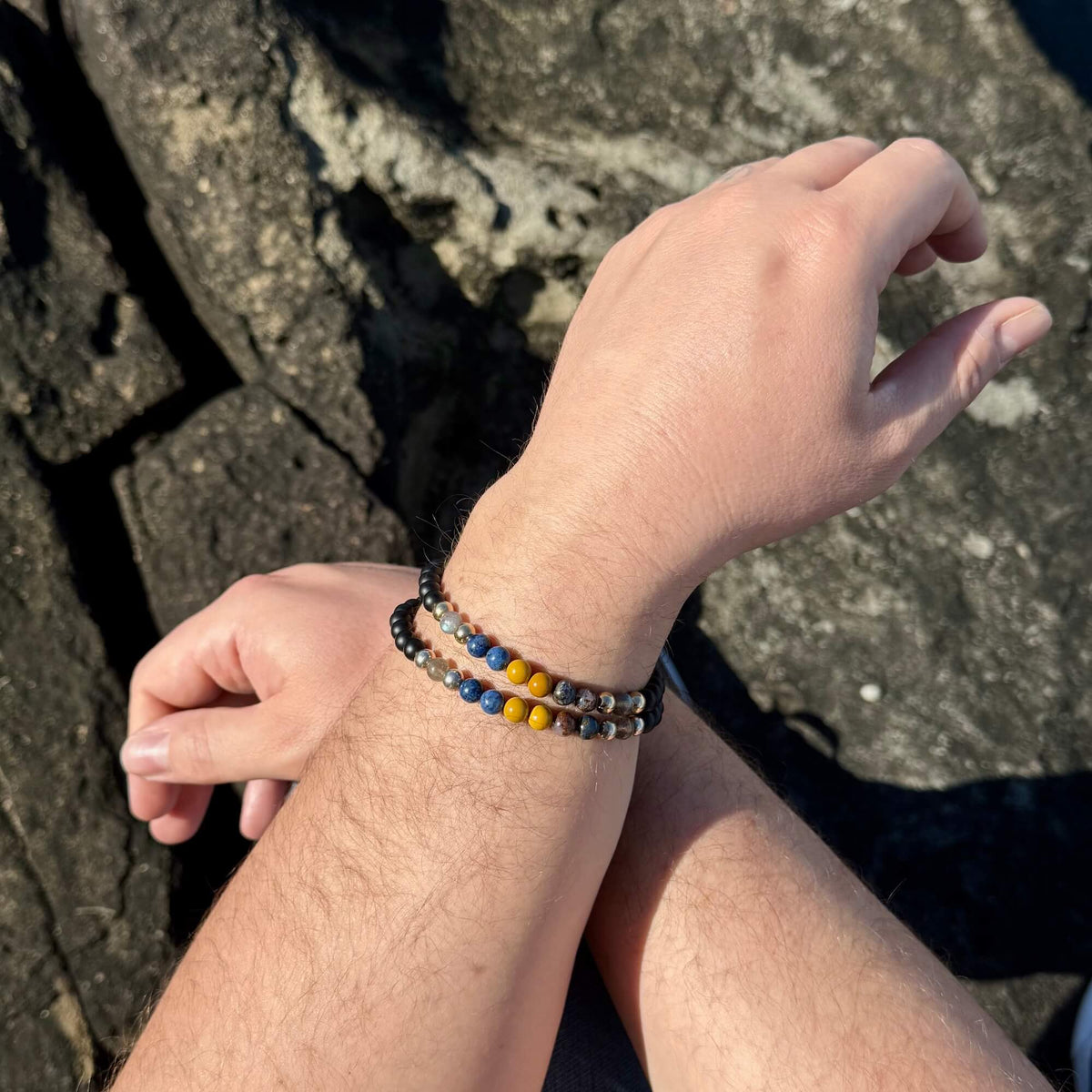 Phoenix Rising bracelet worn on a man's wrist, arms crossed on dark rock