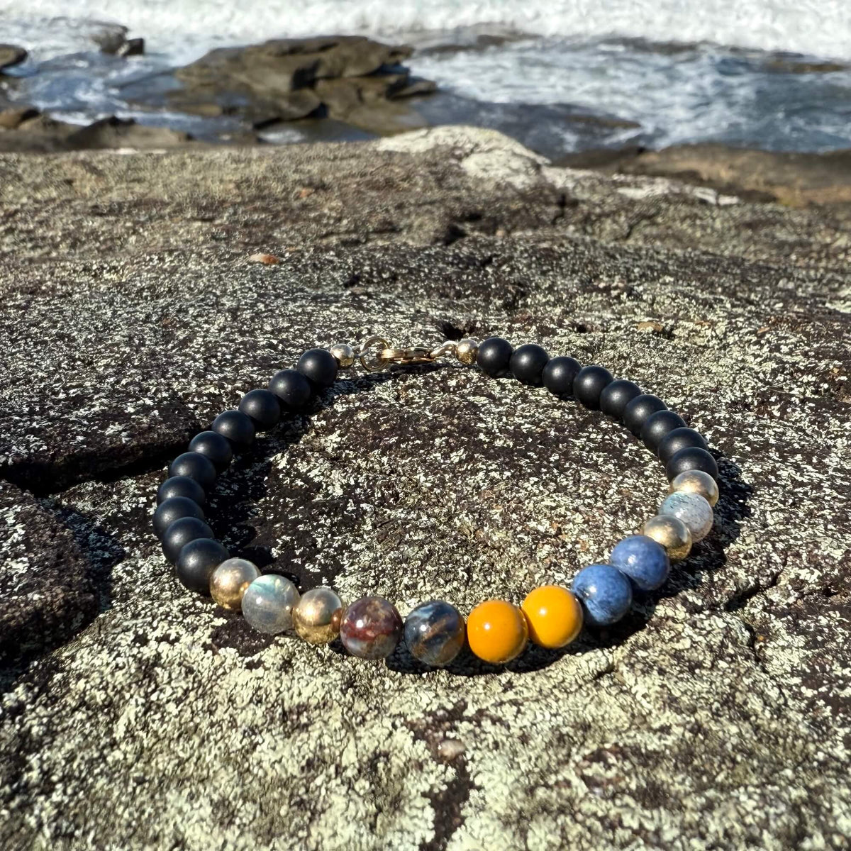 Phoenix Rising five-stone bracelet resting on rock with waves behind