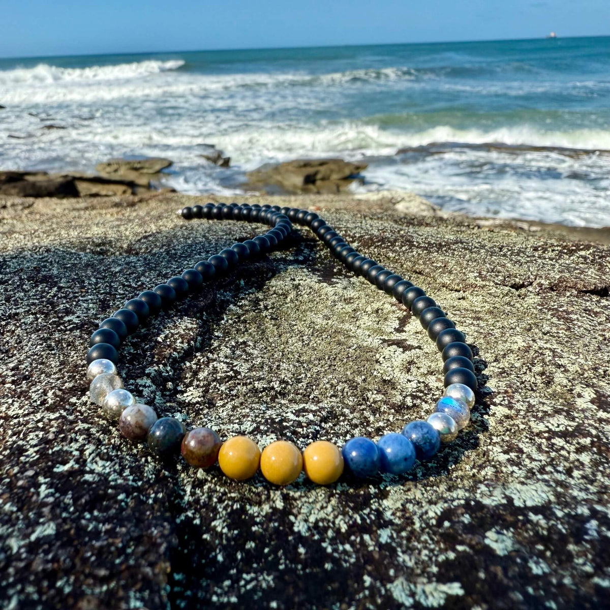 Phoenix Rising necklace on coastal rock under a blue sky