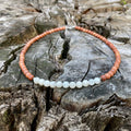 Balance men's necklace: white moonstone with warm natural wood beads, laid on a weathered stump