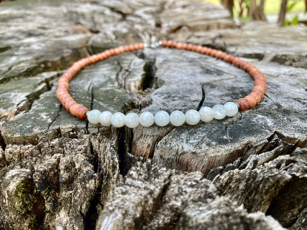 Balance moonstone necklace on old timber with trees behind