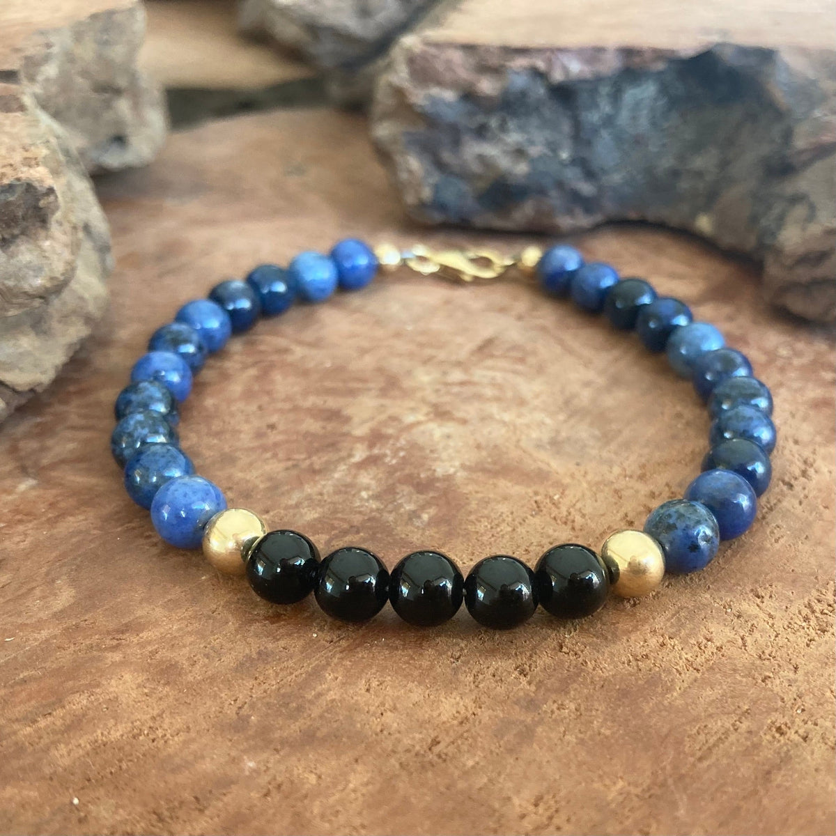 Black onyx beads between gold-fill on The Architect bracelet, resting on timber