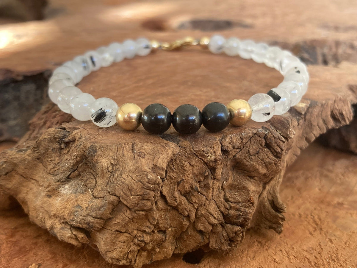 Black shungite beads between gold-fill on The Integrator bracelet, on a driftwood slab