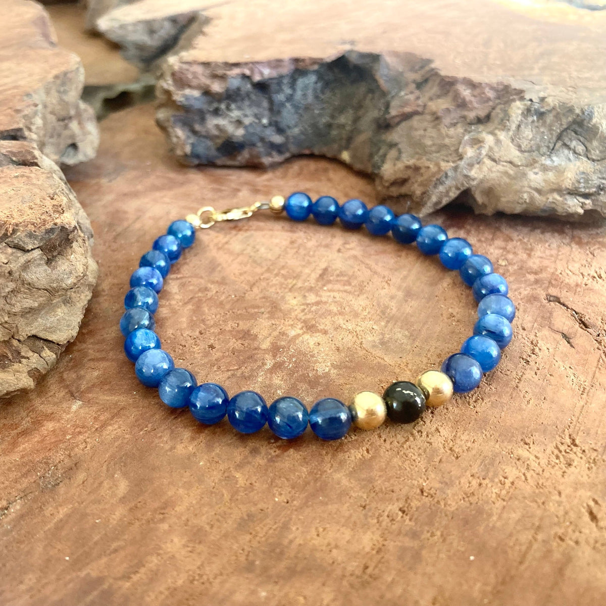 Blue kyanite and shungite bracelet with 14k gold-fill accents and clasp, resting on weathered wood