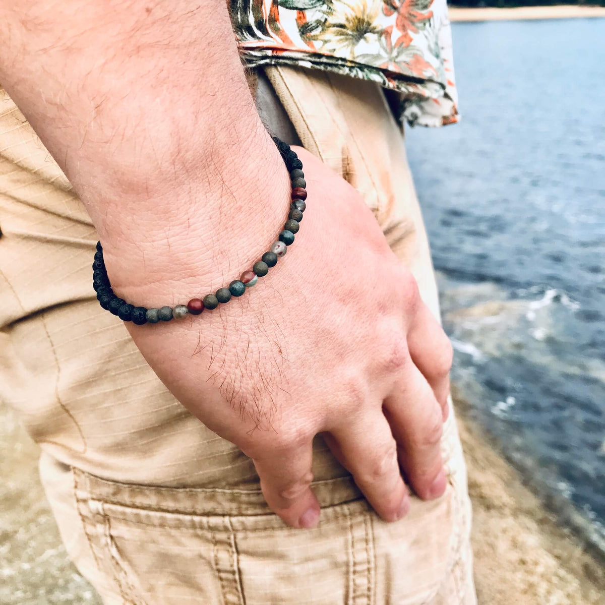 Conviction bracelet on a man's wrist, hand resting on his hip by the water