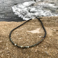 Conviction men's necklace: dark bloodstone and pyrite beads, laid on sandstone by the sea