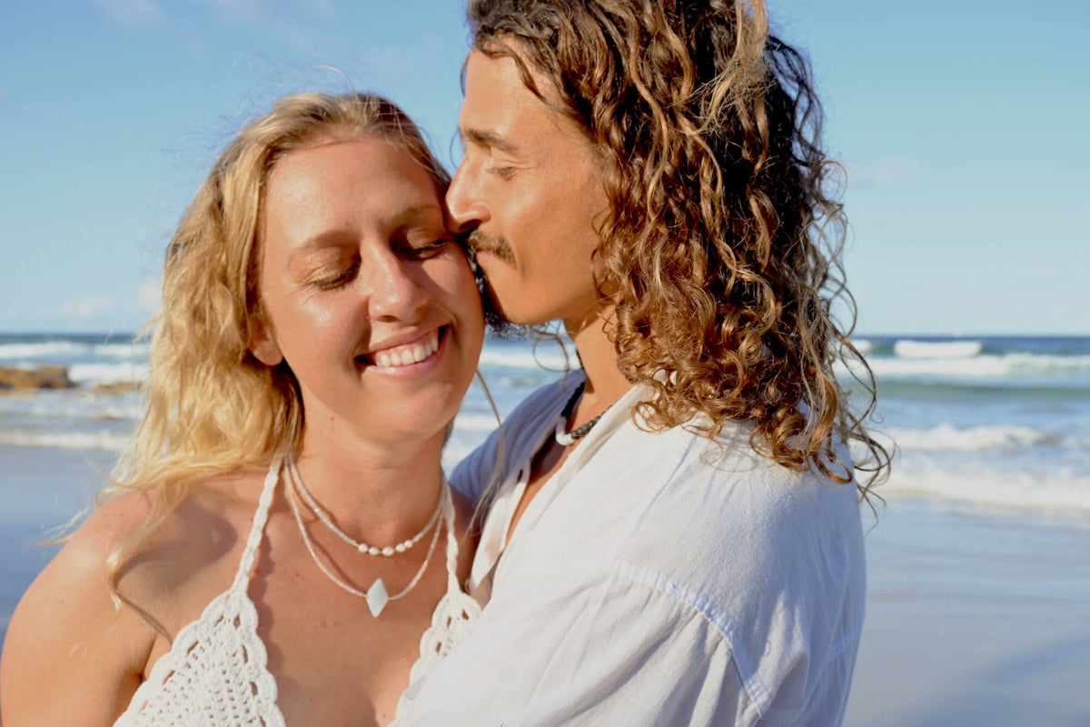 Couple cheek to cheek at the beach, the man wearing the Courage necklace