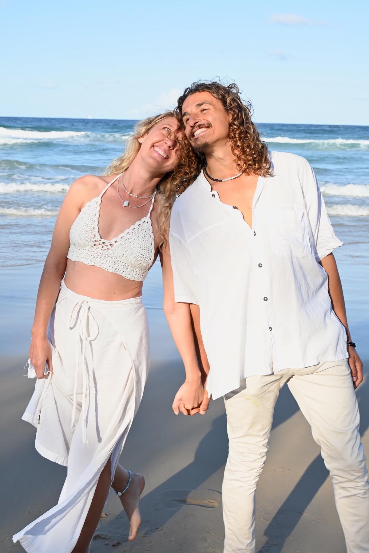 Couple leaning together on the sand, the man wearing the Courage necklace