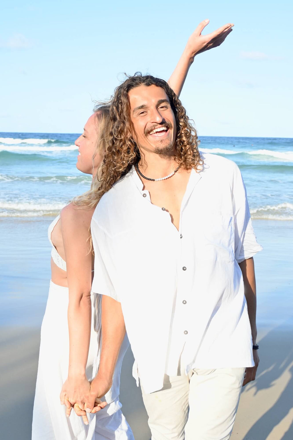 Couple walking hand in hand on the beach, the man wearing the Courage necklace