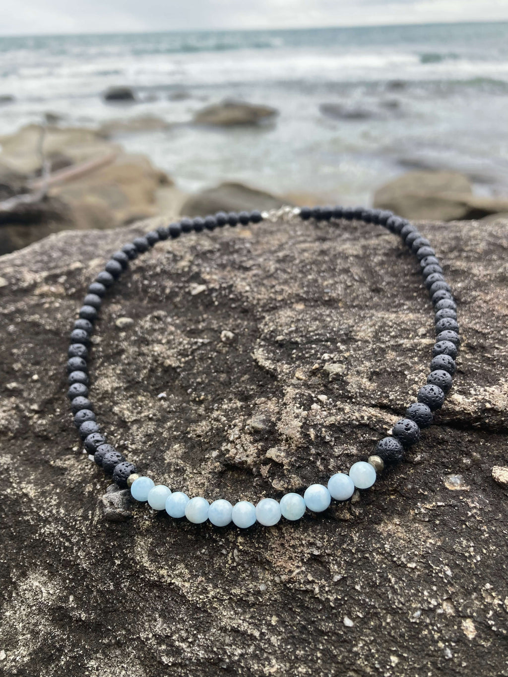 Courage necklace on rock with beach stones behind
