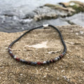 Drive men's necklace: red tiger's eye and grey larvikite beads, on sandstone by the sea
