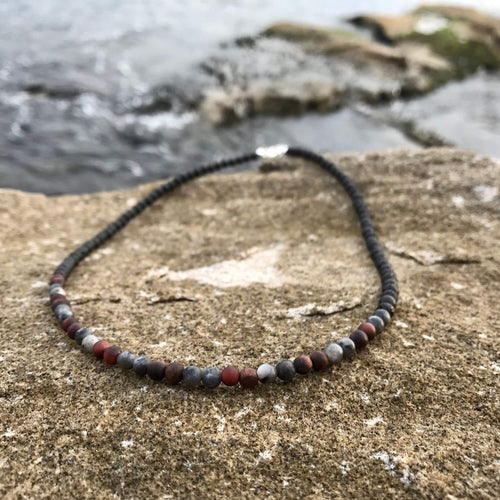 Drive men's necklace: red tiger's eye and grey larvikite beads, on sandstone by the sea