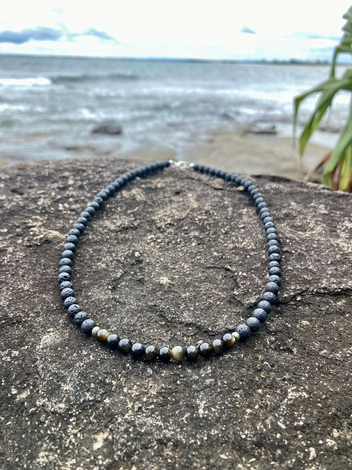 Facing Fears necklace on a rock with the sea behind