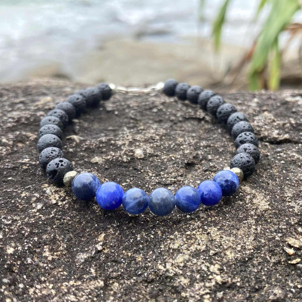 Focus men's bracelet: blue sodalite with matte black lava stone beads, on rock by the sea