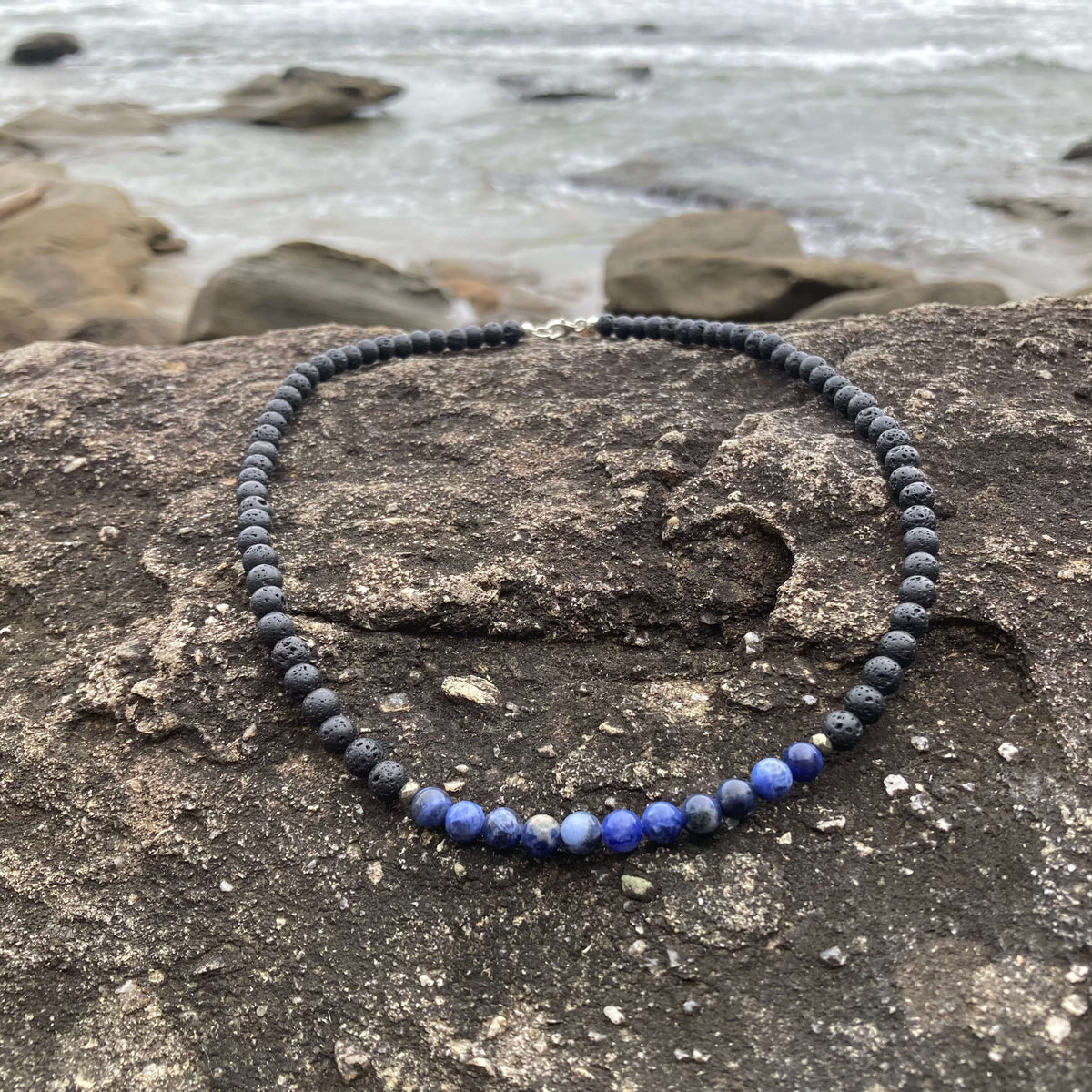 Focus necklace on coastal rock with beach stones behind