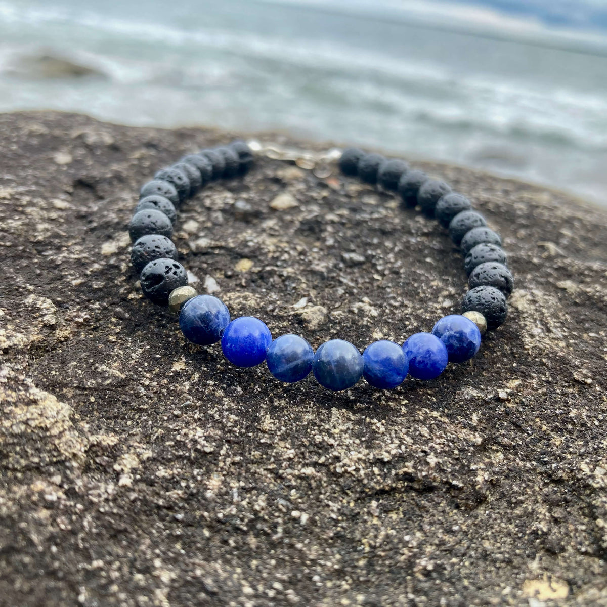 Focus sodalite bracelet on dark rock with the shoreline blurred behind