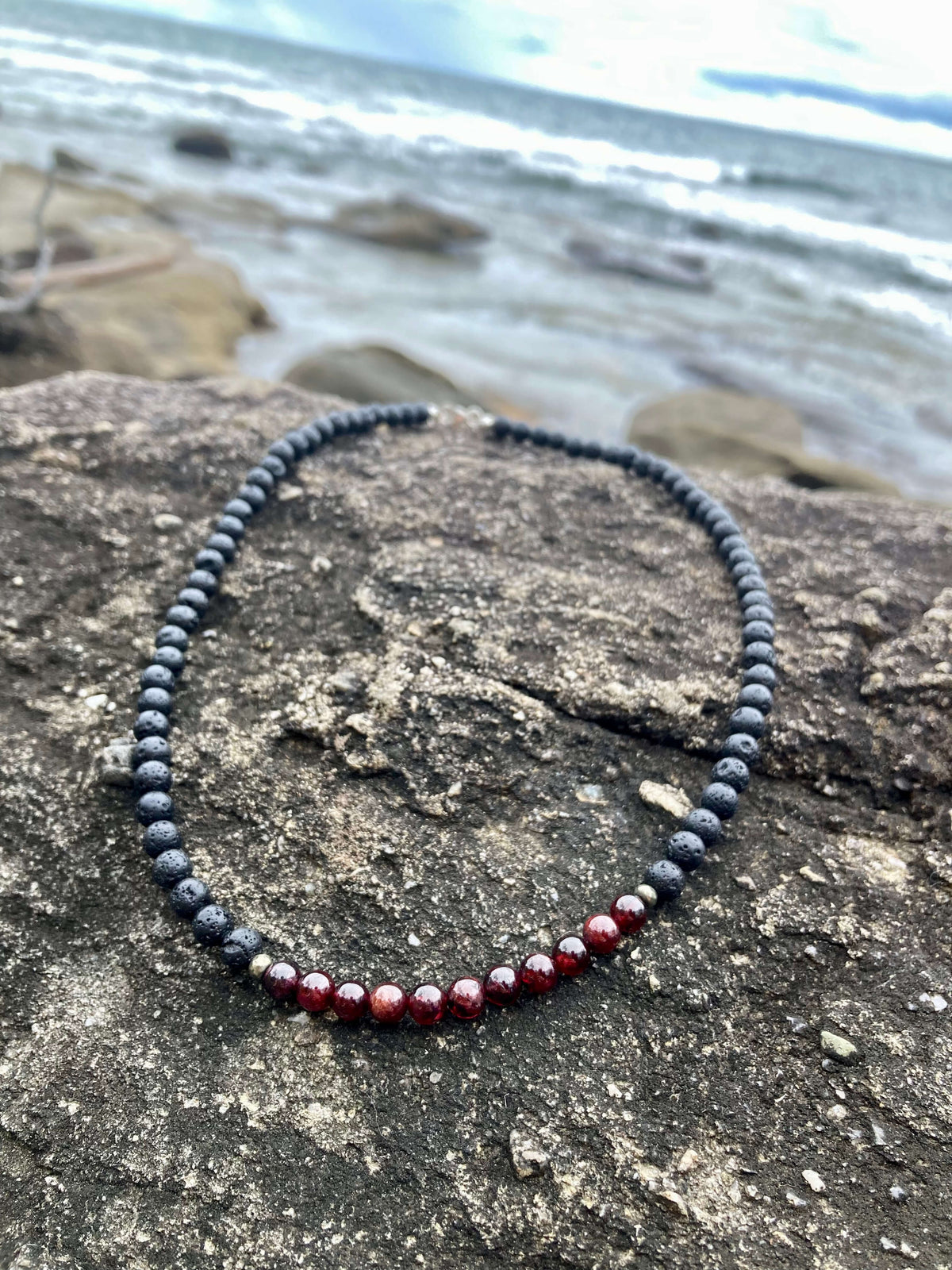 Garnet section of the Prosperity necklace on dark rock with waves behind