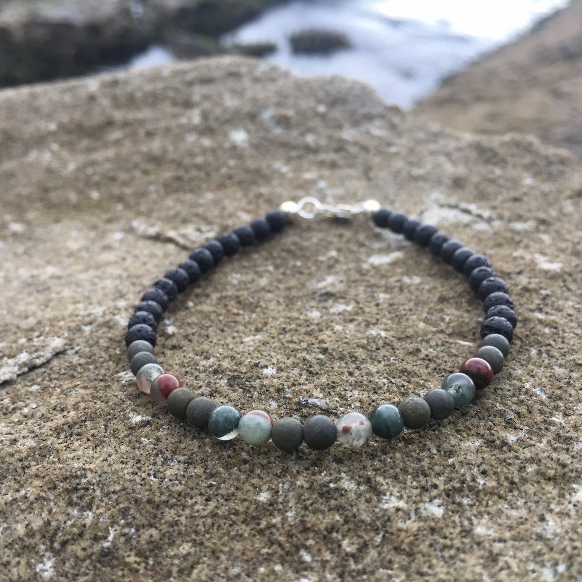 Green-and-red bloodstone beads on the Conviction bracelet, on rock