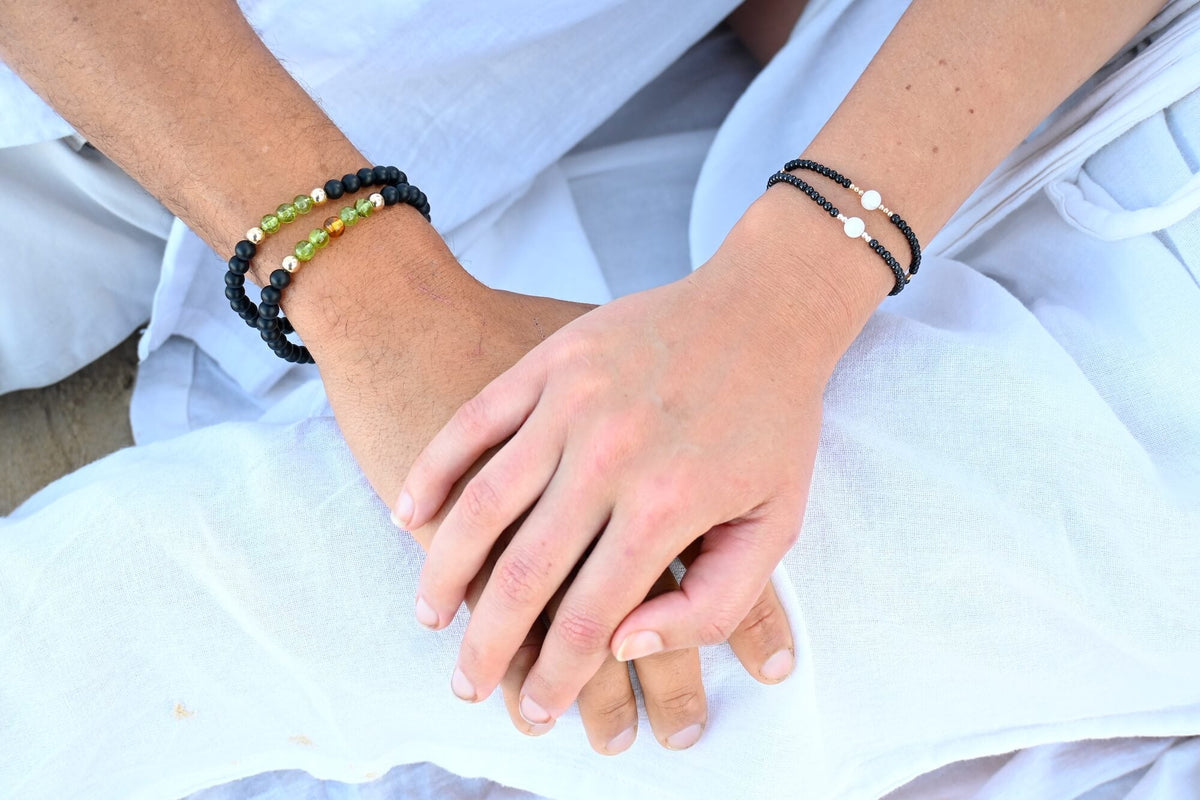 Hands resting on white linen, one wrist wearing The Renewer bracelet