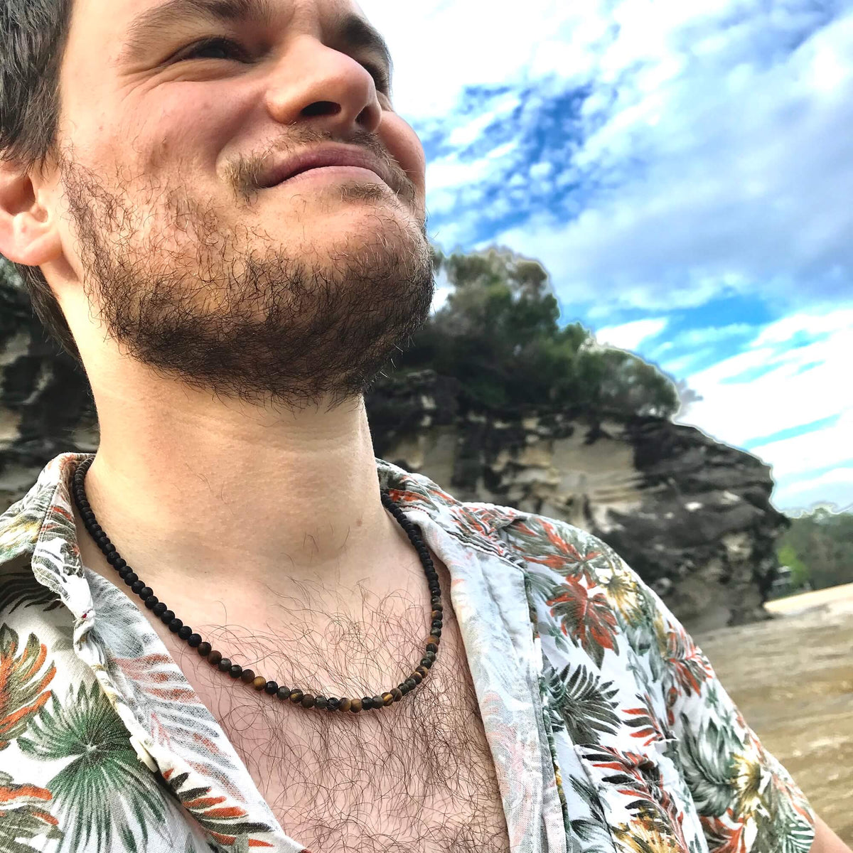 Man in a floral shirt looking up, wearing the Fortitude necklace