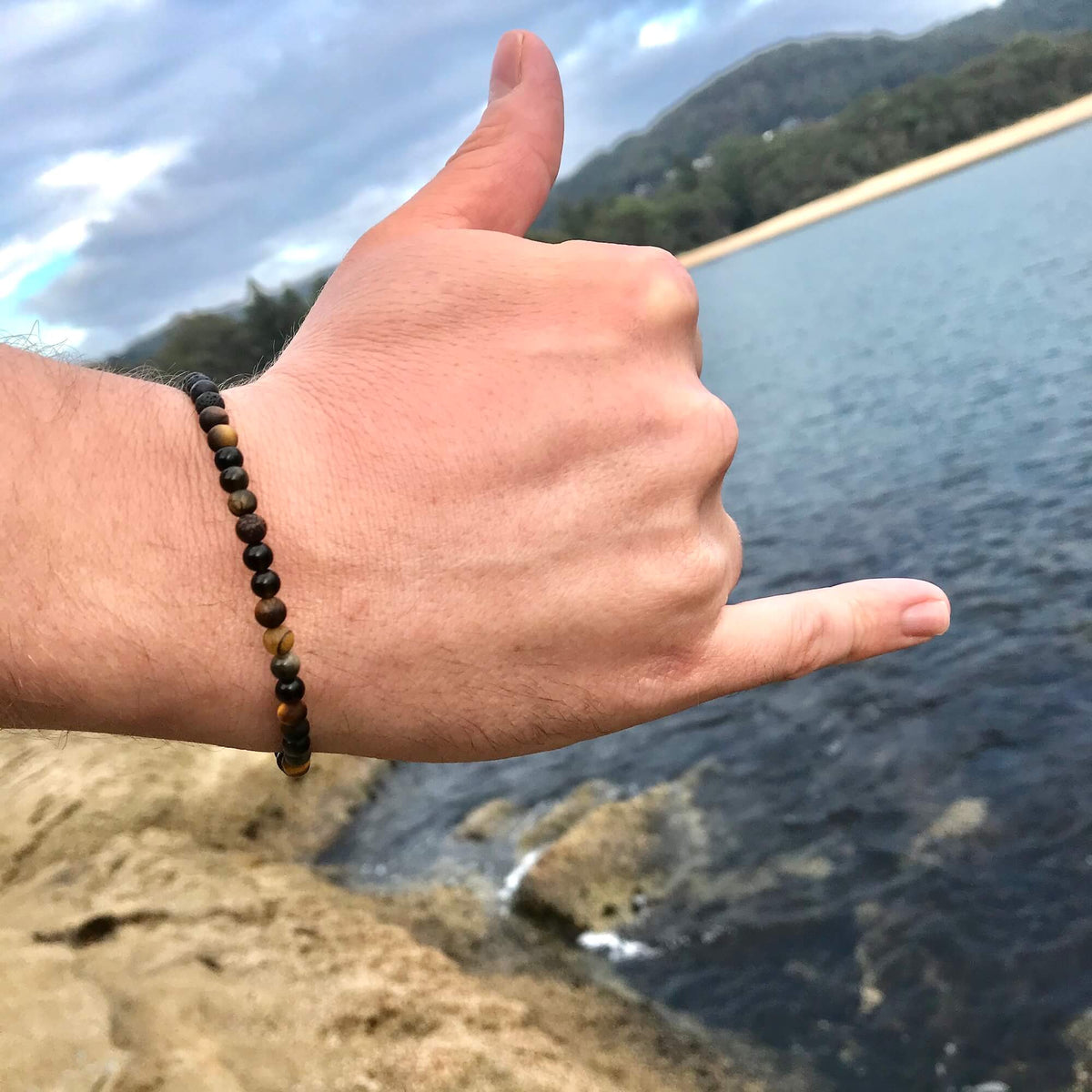Man giving a shaka by the water, wearing the Fortitude bracelet