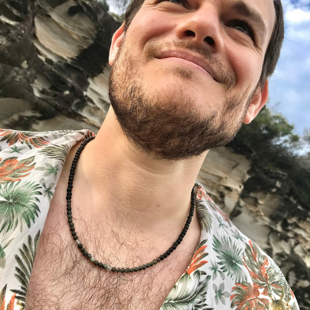 Man looking up, wearing the Conviction necklace with a floral shirt