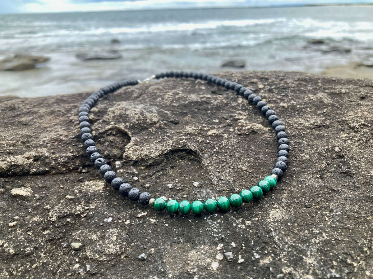 Manifestation necklace on coastal rock with waves behind