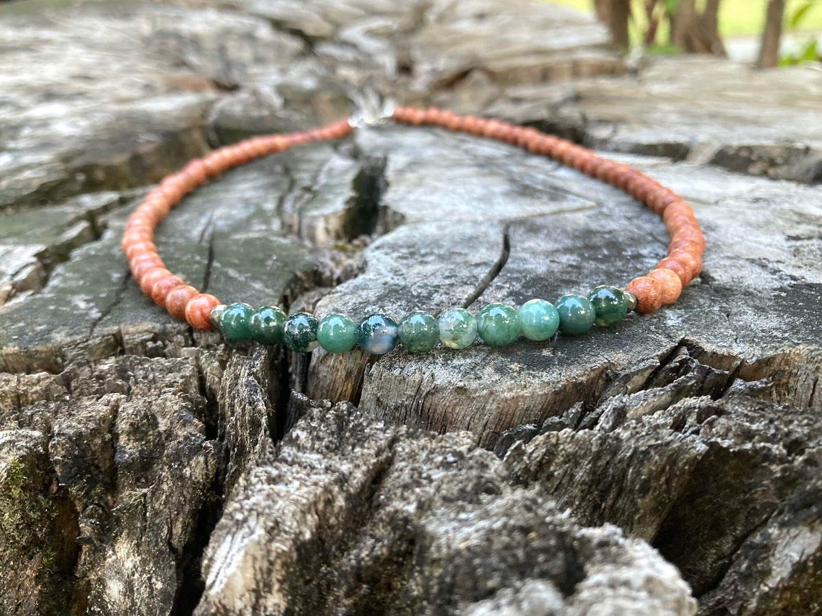 New Beginnings necklace on a cracked tree stump with trees behind