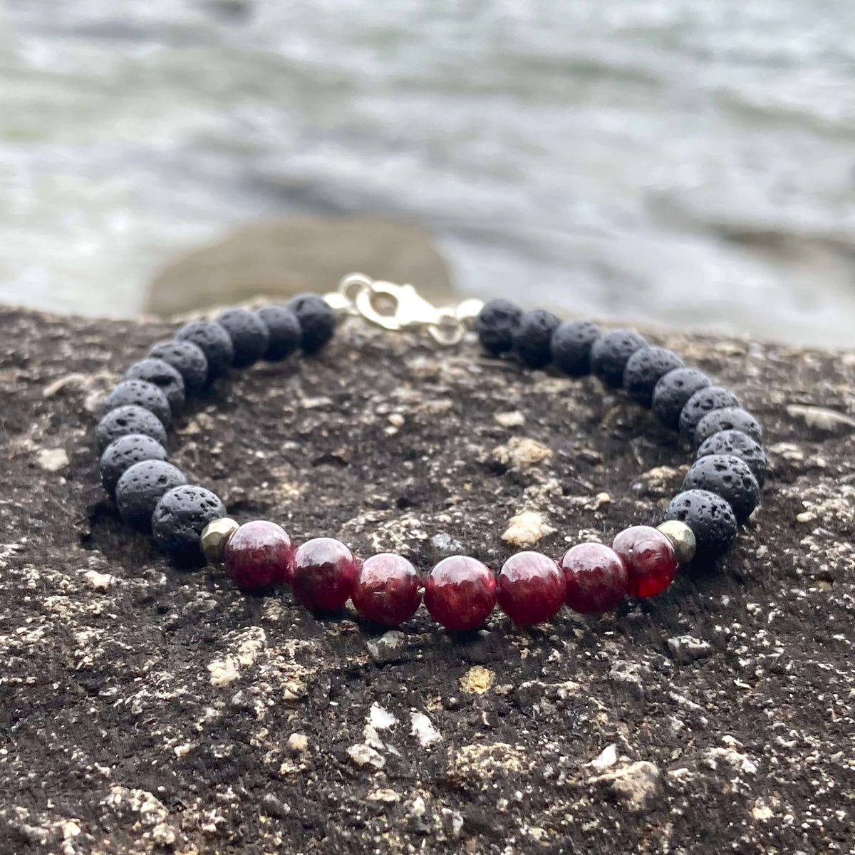 Prosperity garnet bracelet on dark rock with the sea behind