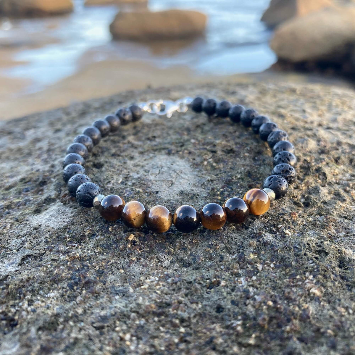 Protection tiger's eye bracelet on dark volcanic rock with rock pools behind