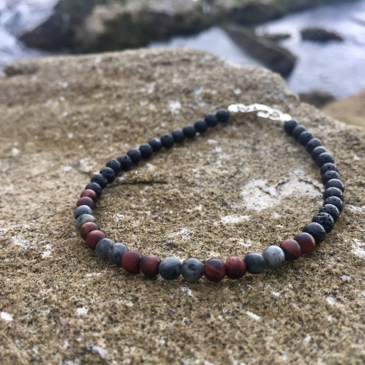 Red tiger's eye beads between larvikite on the Drive bracelet, on rock