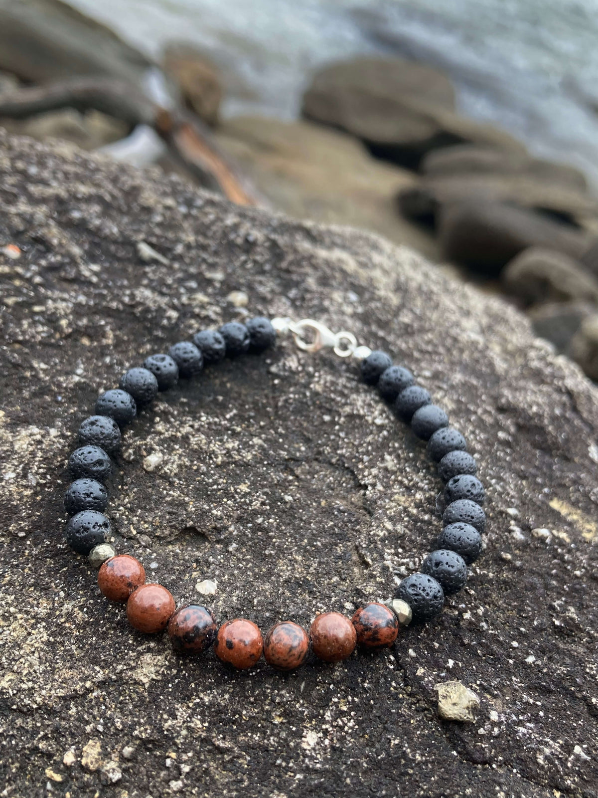 Self-Acceptance bracelet on dark rock with beach stones behind