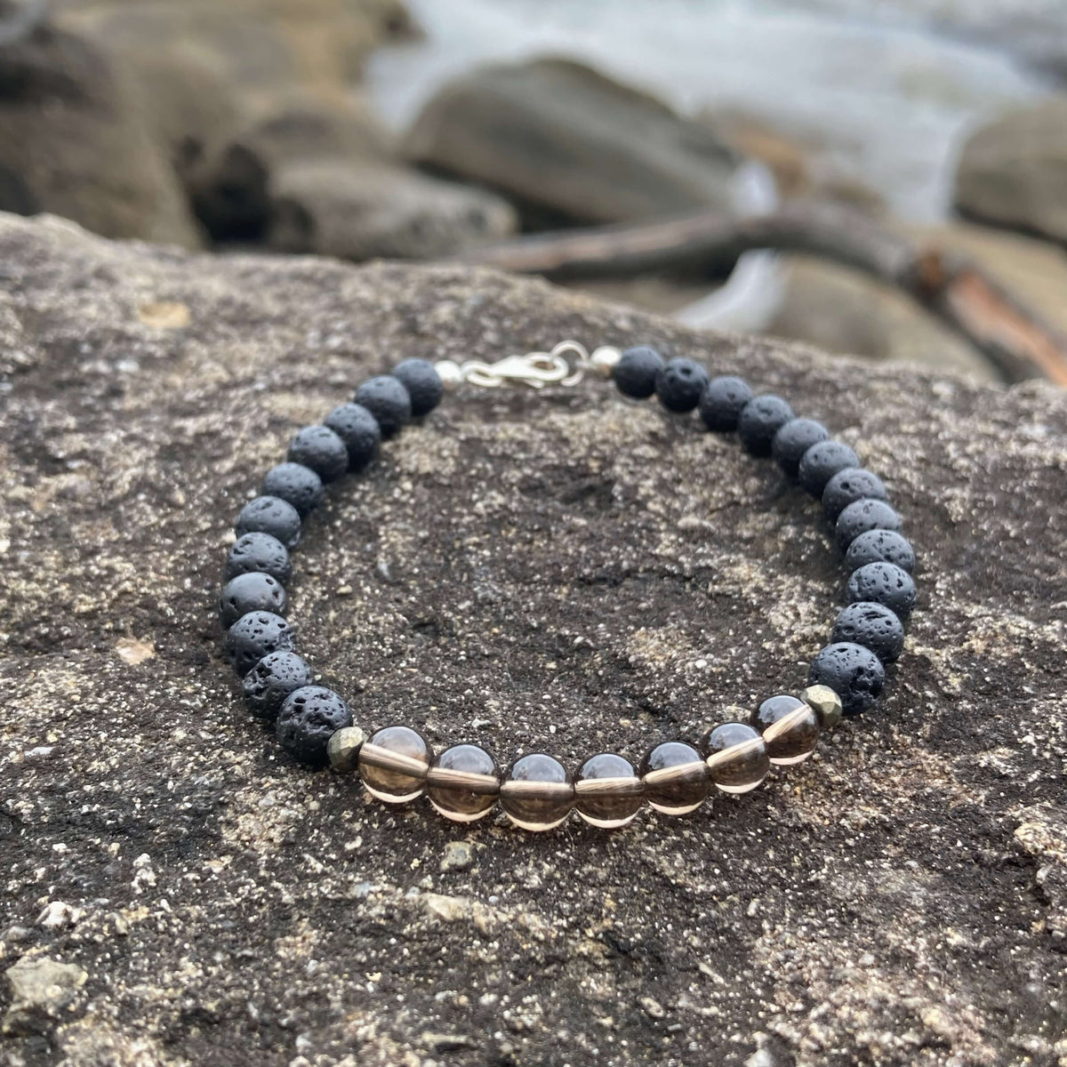 Self-Assurance bracelet on dark rock with the shoreline blurred behind