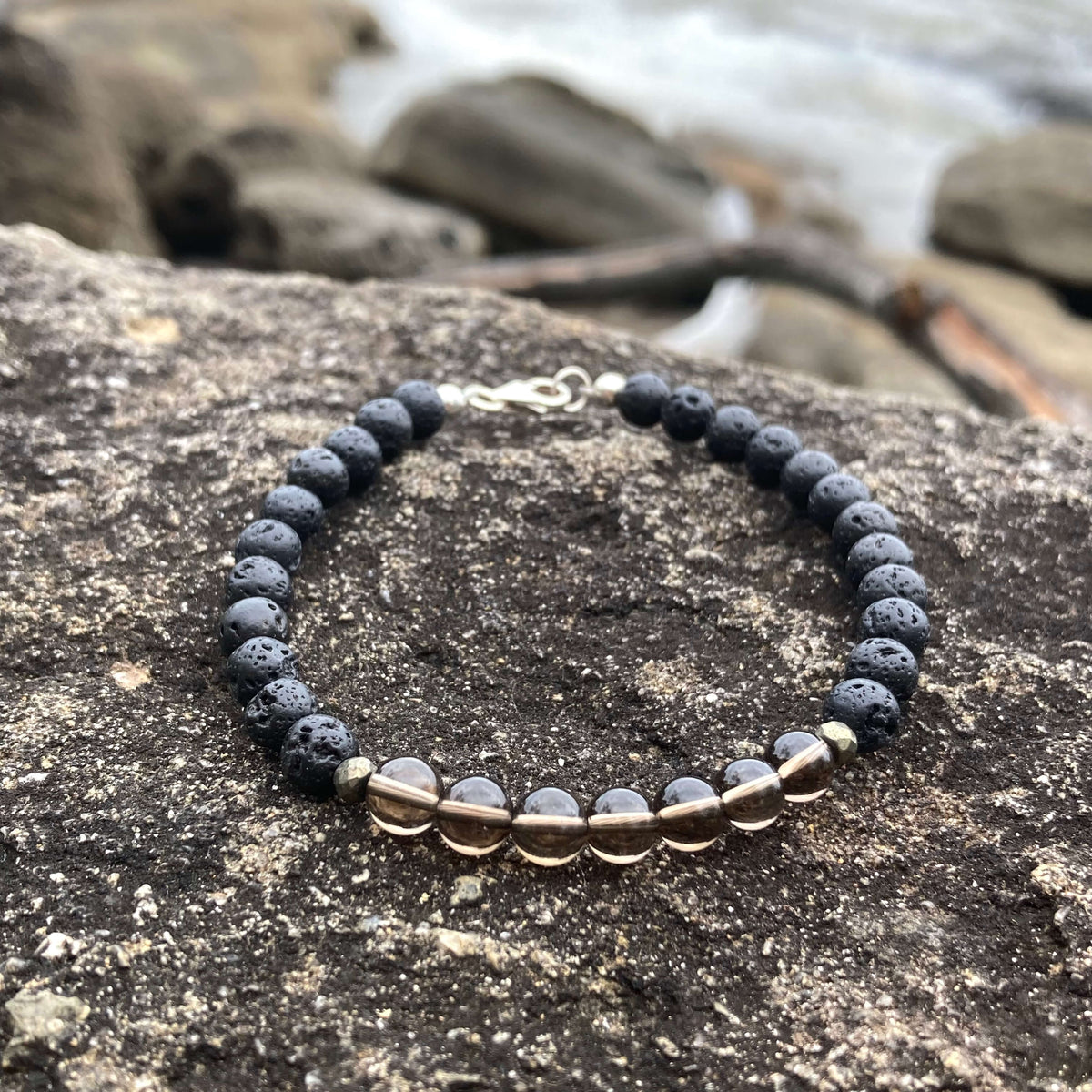 Self-Assurance men's bracelet: translucent smoky quartz with matte black lava stone beads, on rock by the sea