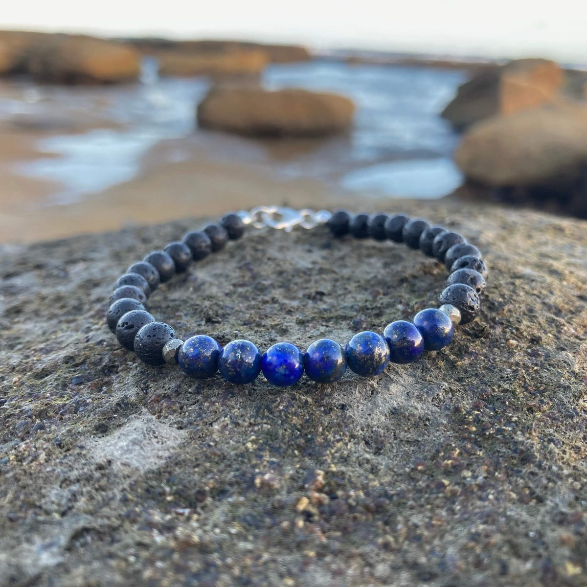 Self-Awareness men's bracelet: deep blue lapis lazuli with dark lava stone beads, on rock by the sea
