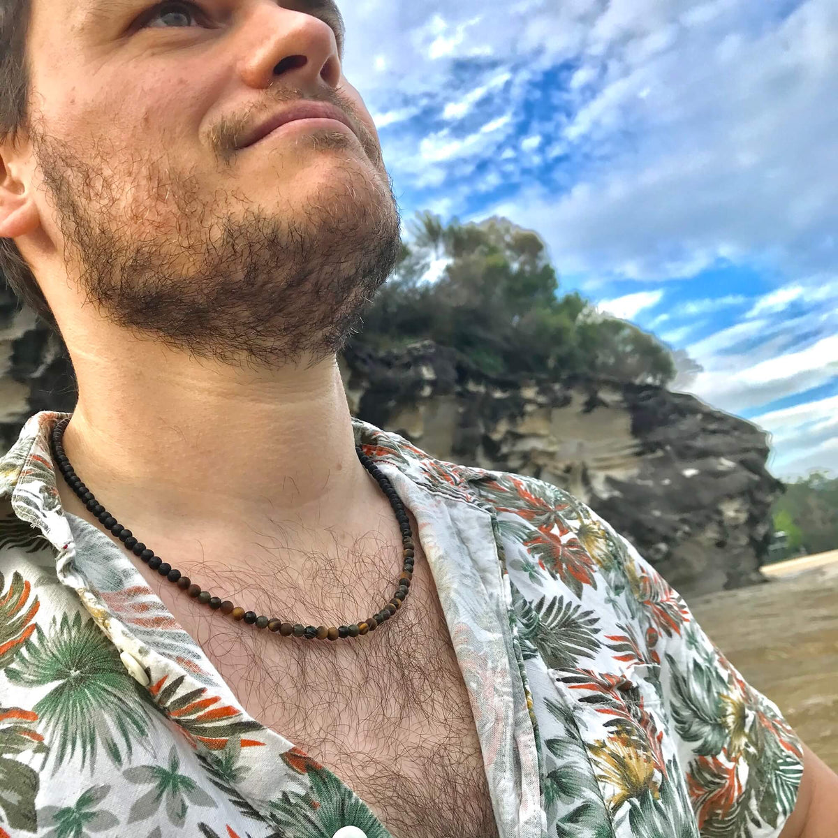 Smiling man under a blue sky wearing the Fortitude necklace