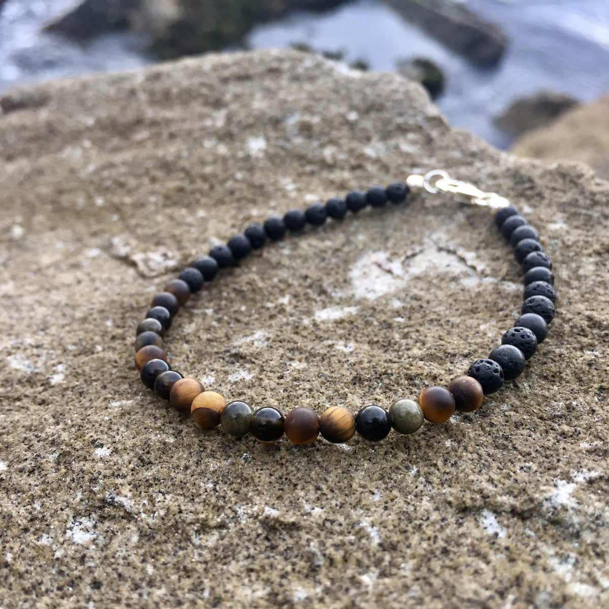 Tiger's eye and golden obsidian beads on the Fortitude bracelet, on rock