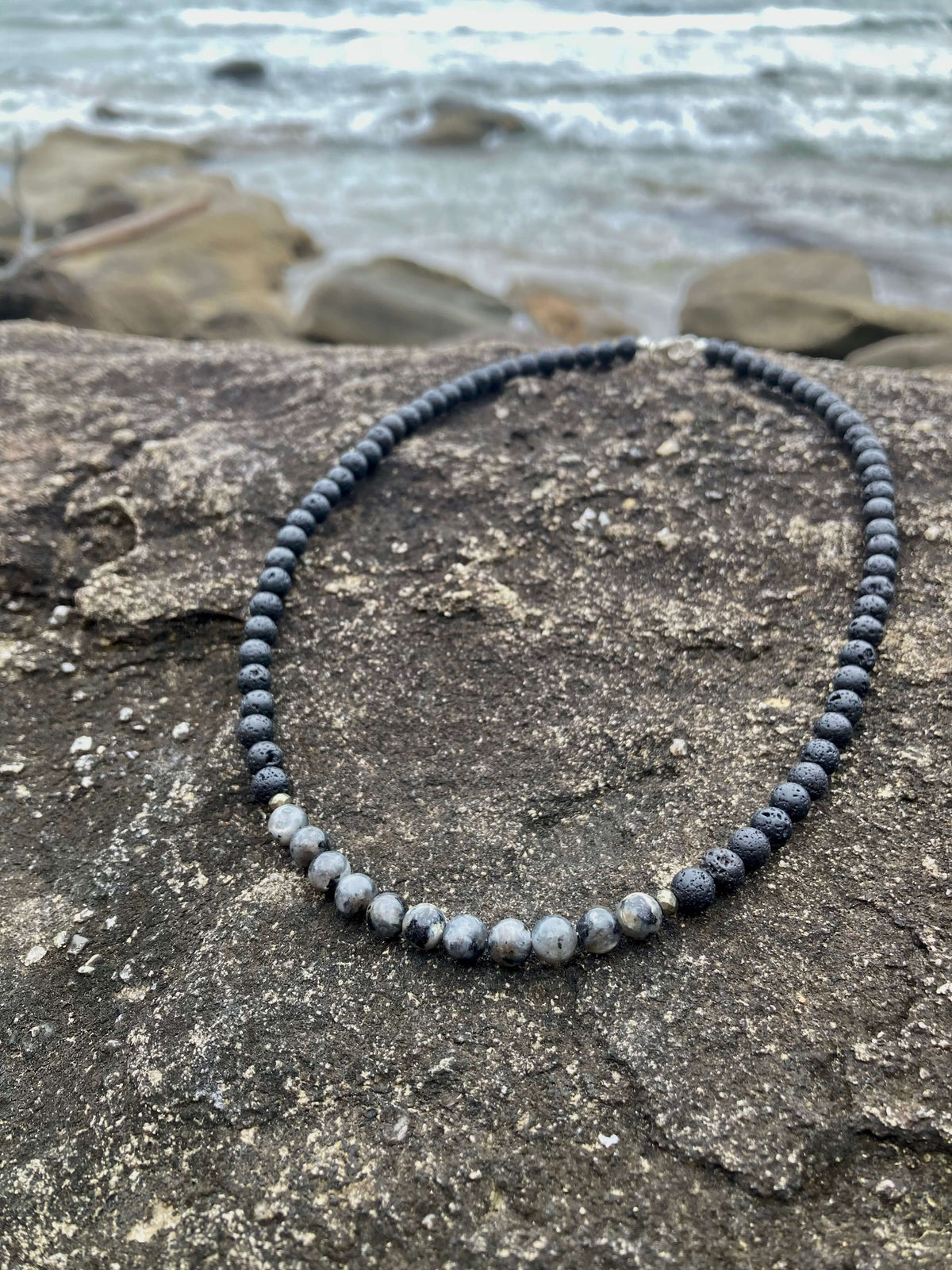 Transformation necklace on coastal rock with beach stones behind
