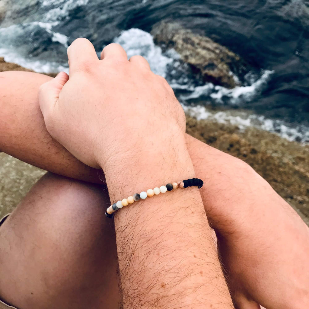 Vitality bracelet on a man's wrist, hands resting on his knee by the sea
