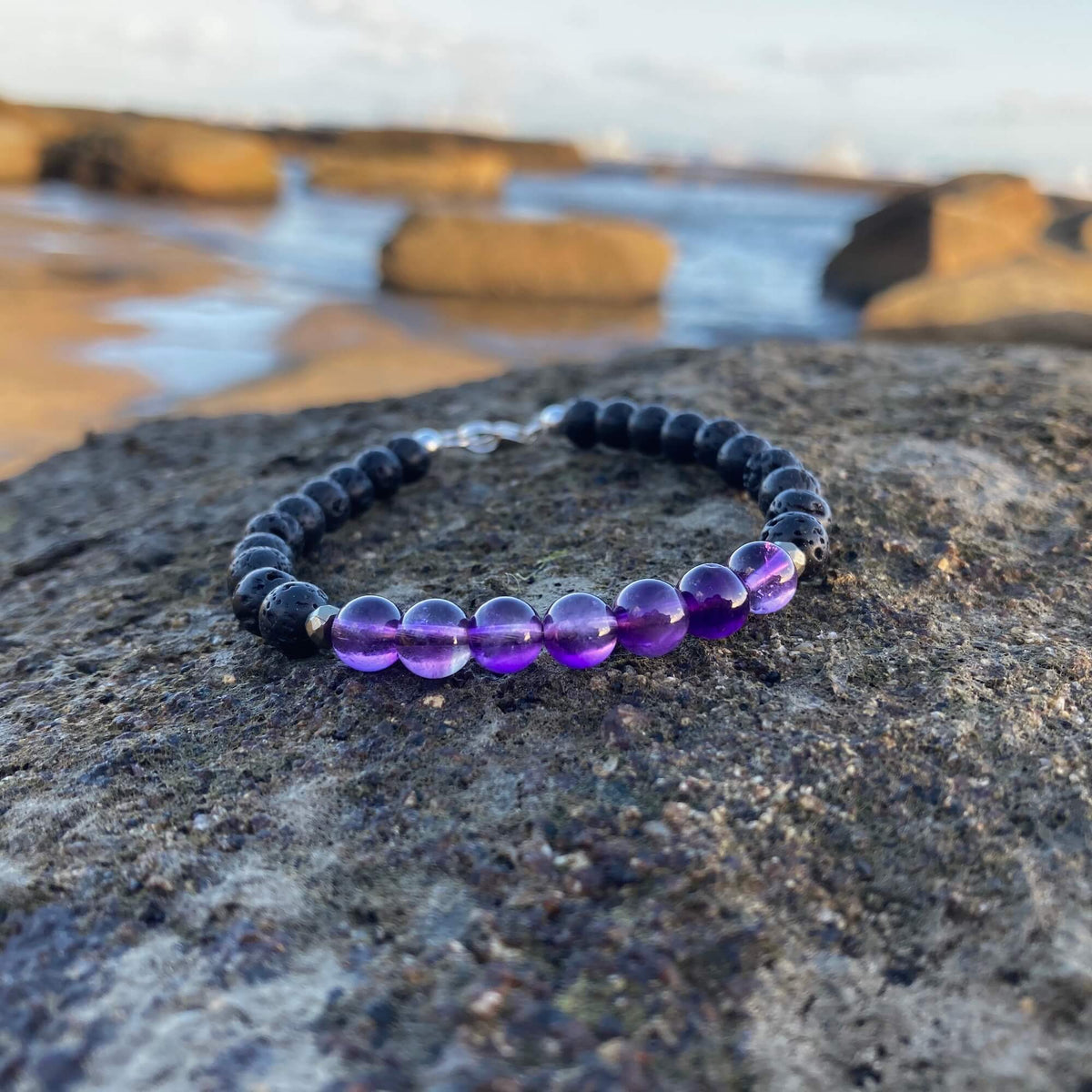 Zen amethyst bracelet on dark rock with rock pools behind
