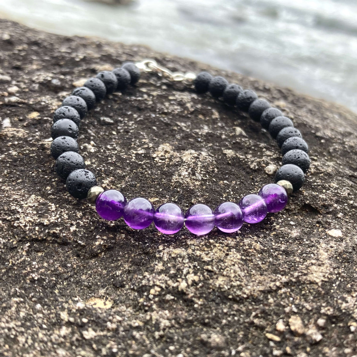 Zen men's bracelet: purple amethyst with matte black lava stone beads, on rock by the sea